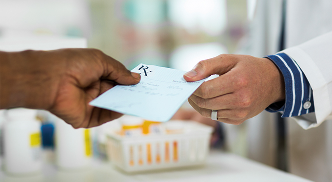 Close-up of two hands holding a prescription pill bottle, with one hand pouring pills into the other. The background is blurred, emphasizing the focus on the hands and the medication.